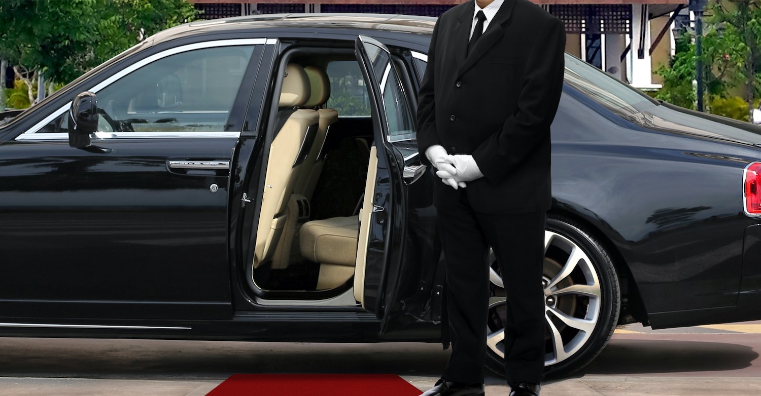 Chauffeur standing by a luxury car with an open door.