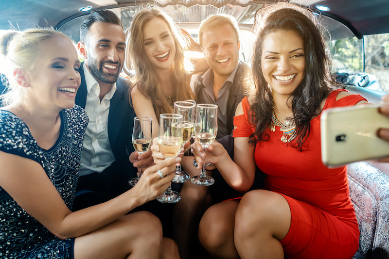 Party people in a limo with drinks taking a selfie with phone smiling into the camera