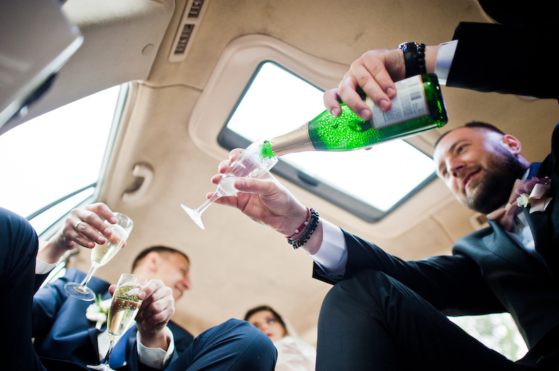Groomsman opening the bottle and pouring champagni into glasses in the car.