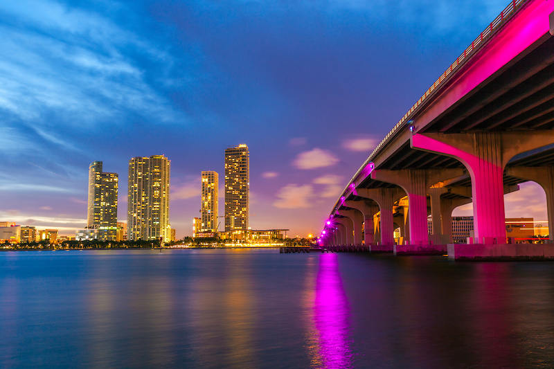 Miami city skyline panorama at dusk with urban skyscrapers and bridge over sea with reflection